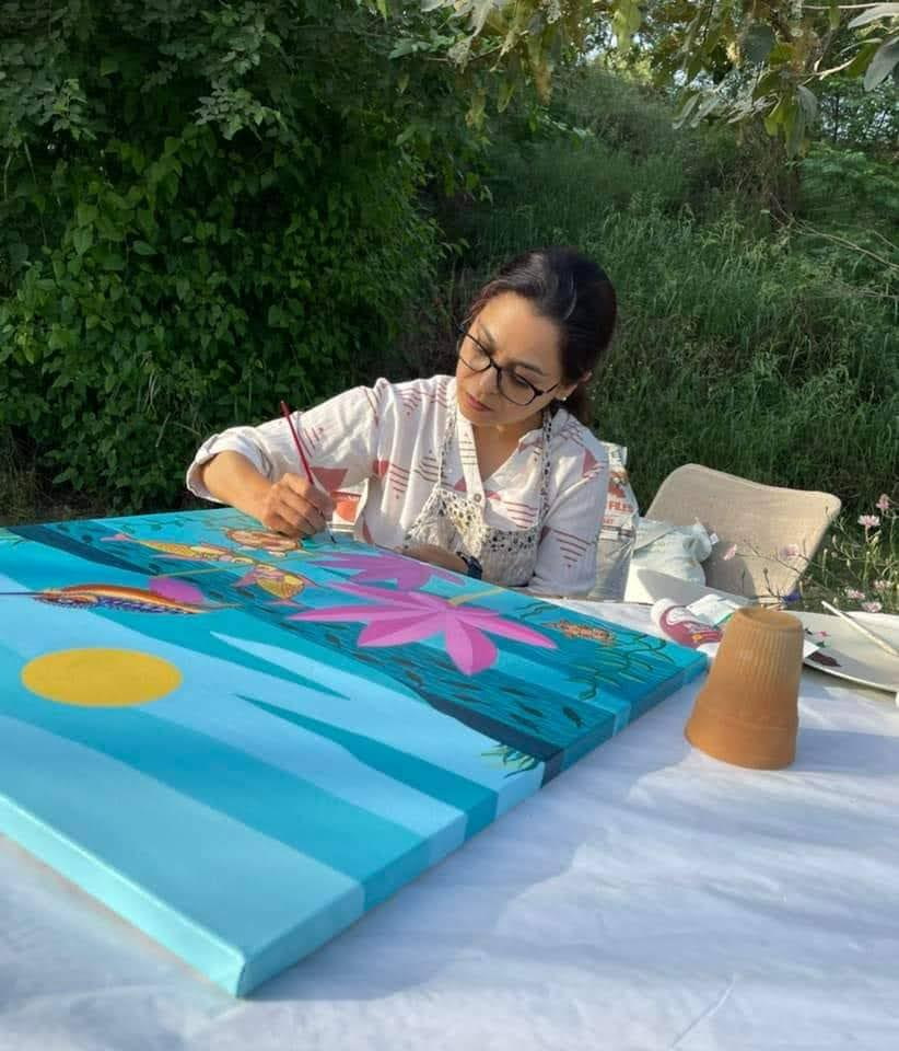 Pavit painting outdoors on a turquoise canvas filled with pink lotus flowers, birds and fish.